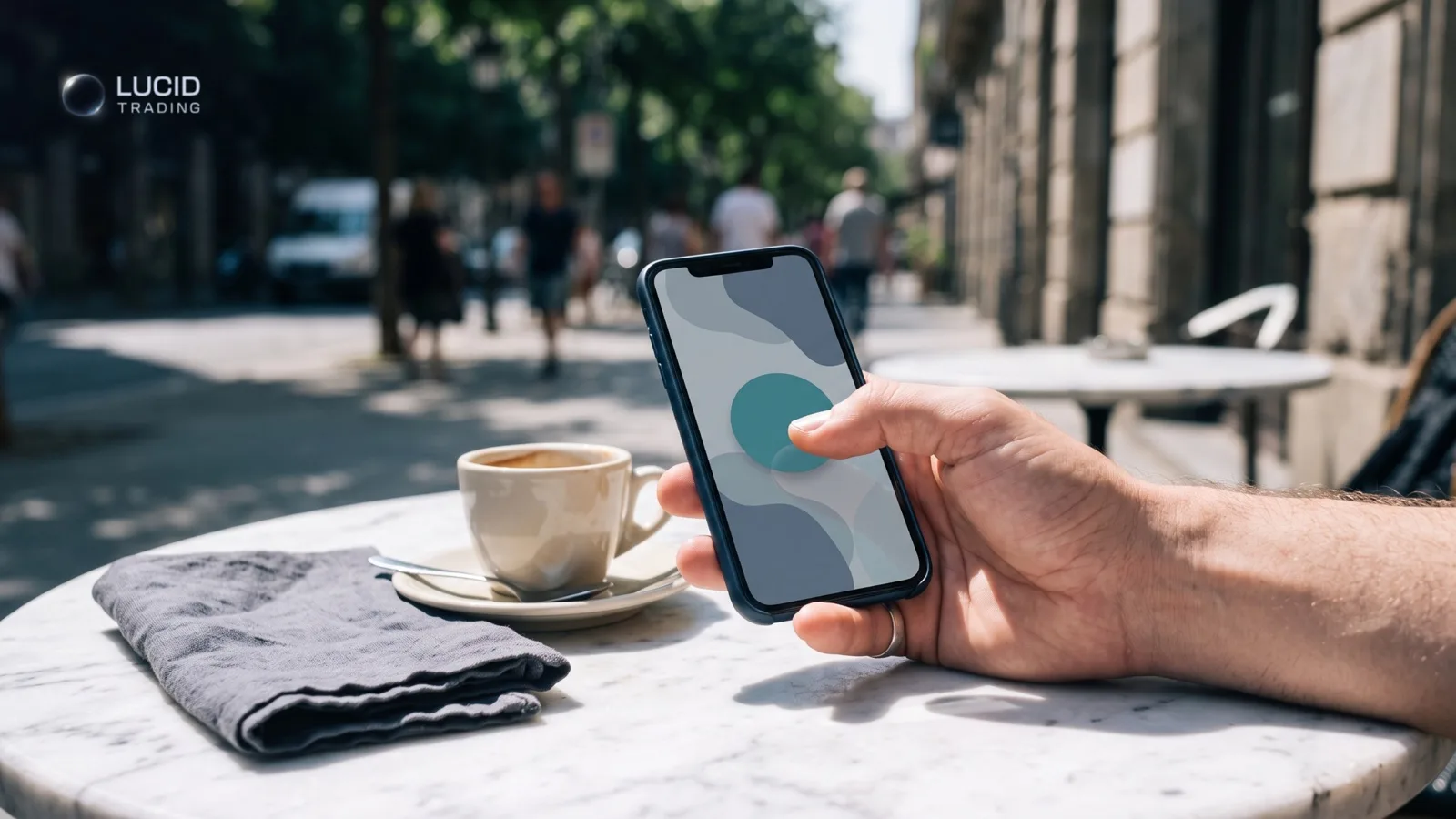 A hand holding a phone at a sunlit cafe table at midday, picturing a Lucid Trading on-demand payout request made during the session